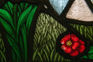 A close-up of a stained glass window with green foliage and a red flower