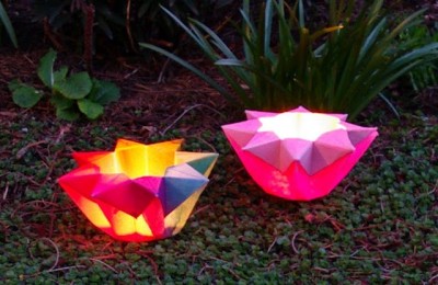 A photo of two origami paper lanterns, one pink and one yellow and red. They are lit from within but the rest of the photo is in darkness so they are glowing.