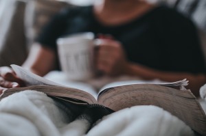 A close-up photo of someone reading a book with a cup of tea. The large book is lying open on their lap and the cup is resting on it.